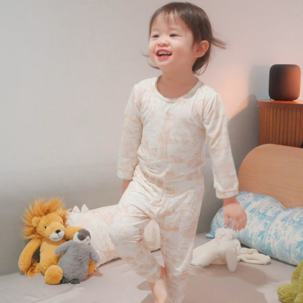Child in bamboo pyjamas sitting on a bed with stuffed animals — soft, breathable, eczema-friendly sleepwear.