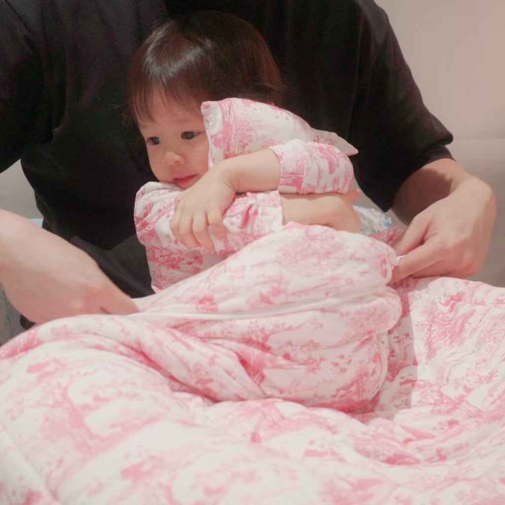 Infant wrapped in a pink bamboo baby blanket being held by an adult against a neutral background — soft, breathable, eczema-friendly fabric.
