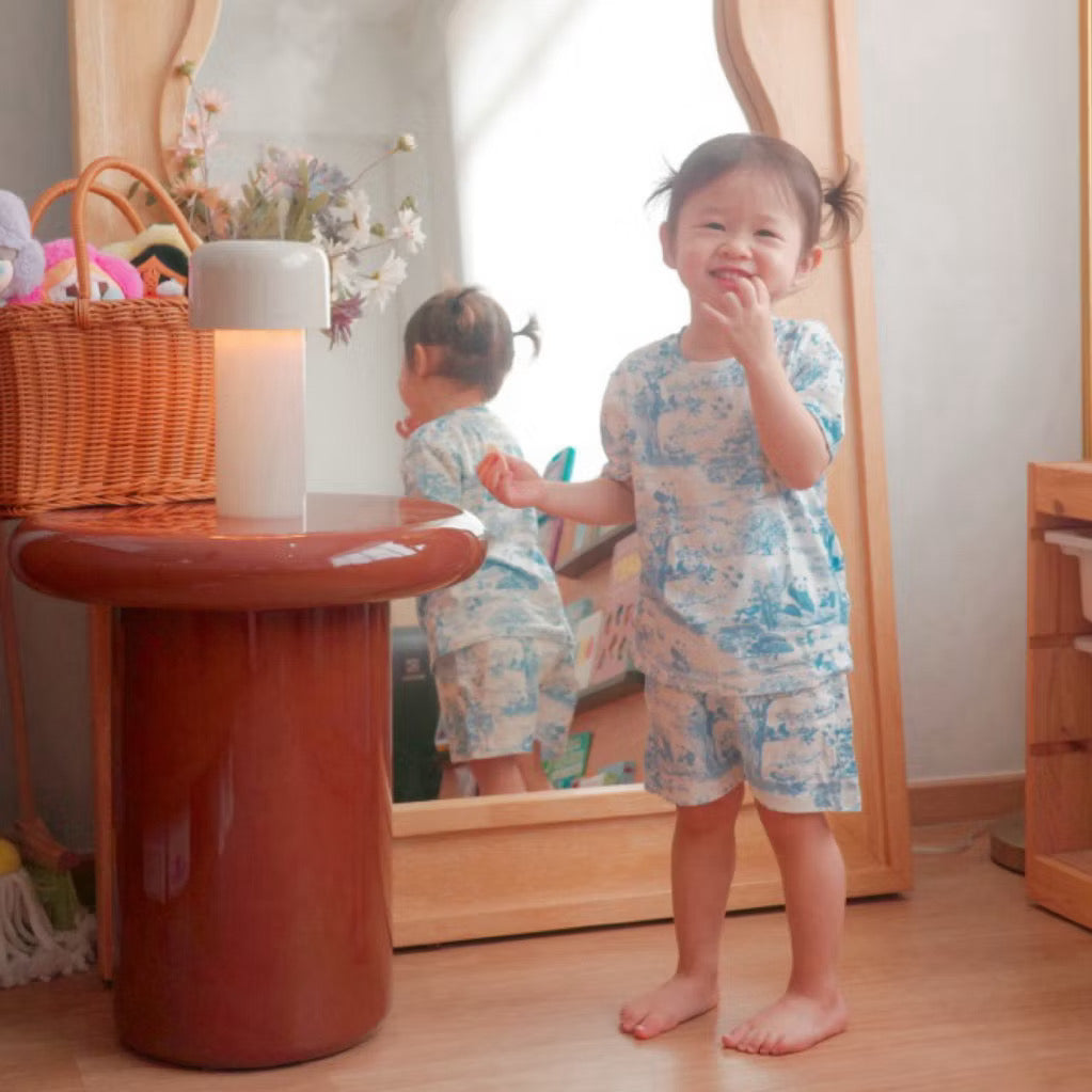 Child wearing a blue short sleeve 2-piece bamboo kids pyjamas set standing in front of a mirror and smiling — cooling, eczema-friendly sleepwear.