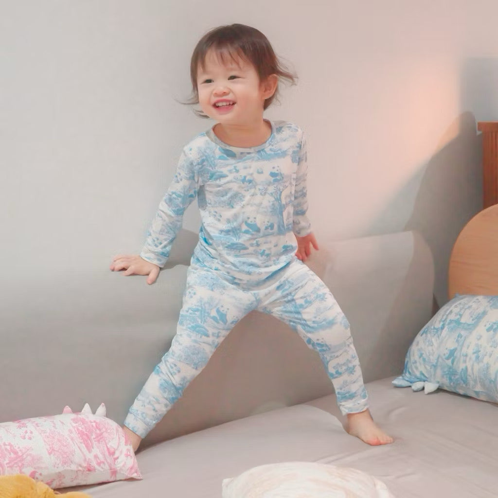Child wearing a blue and white 2-piece bamboo kids pyjamas set sitting on a bed — cooling and eczema-friendly sleepwear in Singapore
