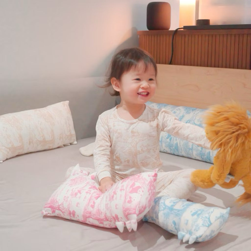 Child in pink bamboo pyjamas sitting on a bed with colorful pillows while hugging a lion plush toy — cooling, soft, eczema-friendly sleepwear.