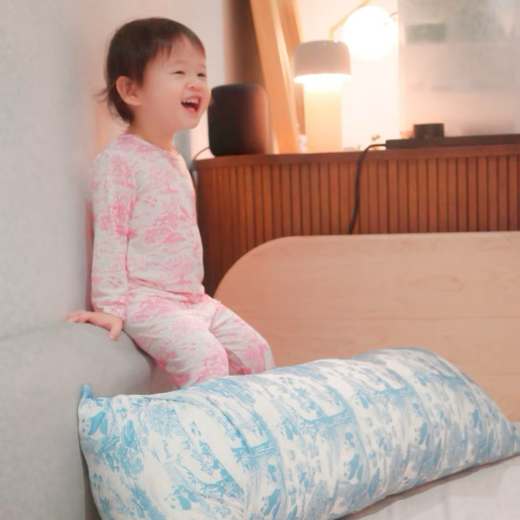 Child wearing pink bamboo kids pyjamas sitting on a bed beside a blue and white patterned pillow — eczema-friendly sleepwear in Singapore.