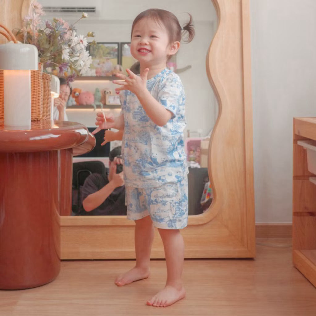 Child wearing a pink short sleeve 2-piece bamboo kids pyjamas set standing in a room with wooden furniture and a mirror — cooling and eczema-friendly sleepwear