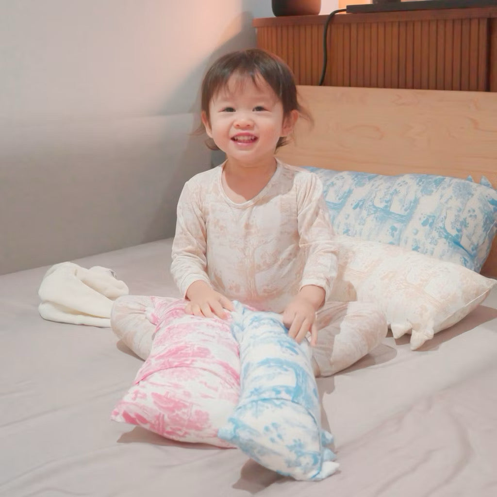 Child in bamboo kids pyjamas sitting on a bed with colorful pillows and a soft toy — cooling, eczema-friendly sleepwear.