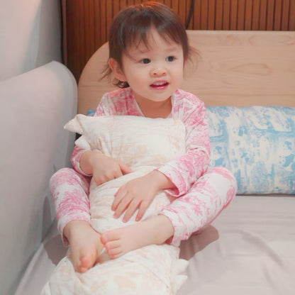 Child in pink bamboo pyjamas sitting on a bed while holding a white pillow with a beige pattern — soft, cooling, eczema-friendly sleepwear and bedding.